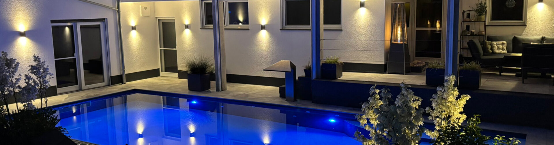 Beleuchteter Swimmingpool auf moderner Terrasse bei Nacht